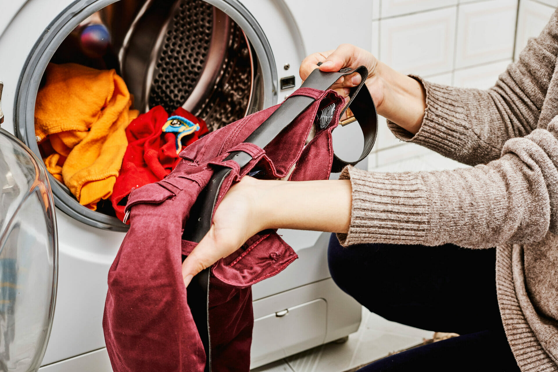 A pair of hands loading clothes into a washing machine